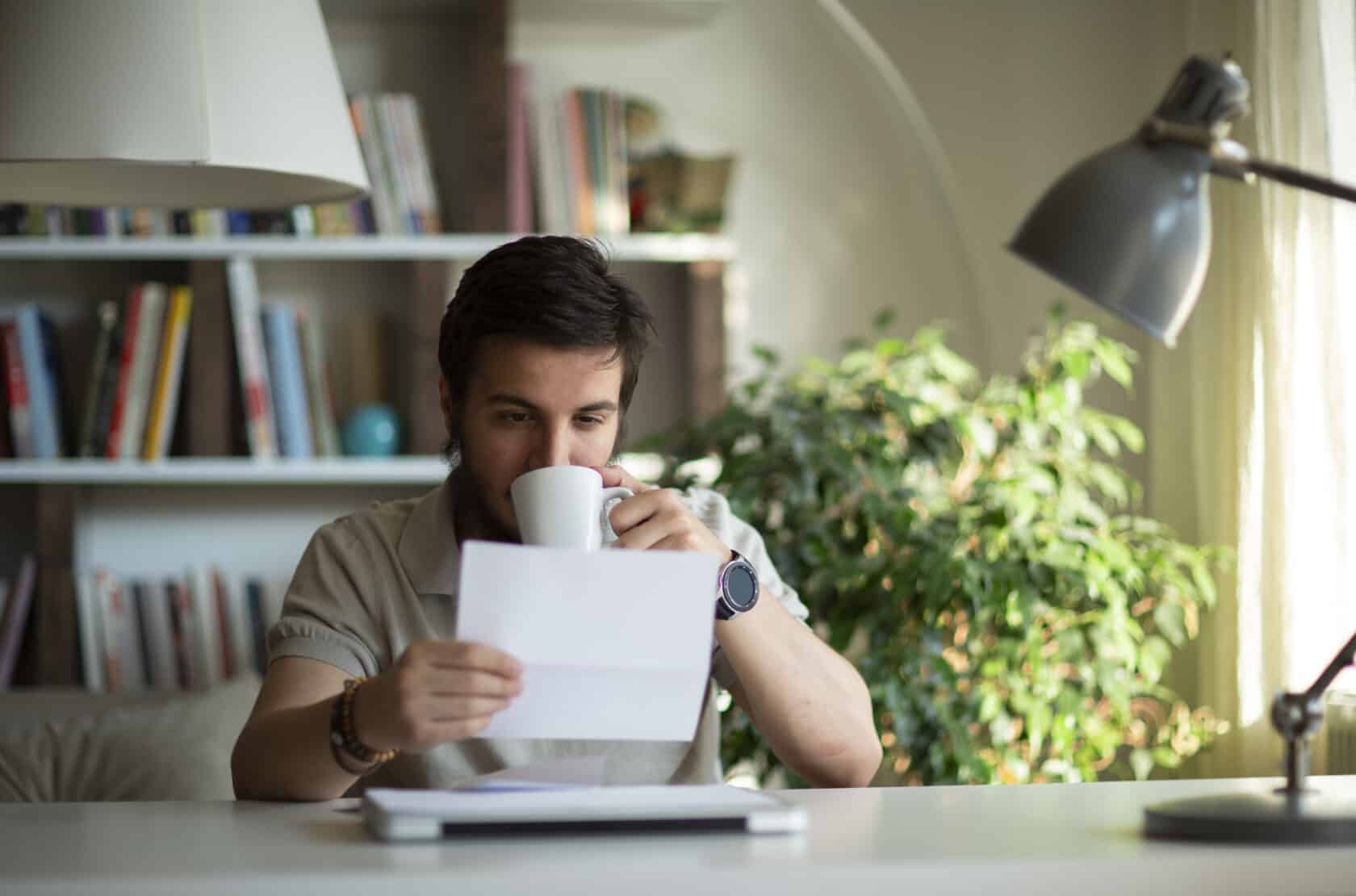 Mann trinkt Kaffee und schaut dabei auf ein Blatt Papier.