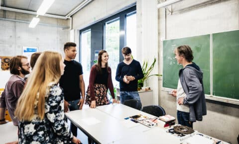 Schüler stehen mit Lehrer im Kreis und dieser erklärt ihnen etwas.