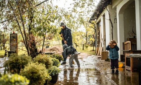 Vater und Kinder räumen im Regen vor dem Haus auf