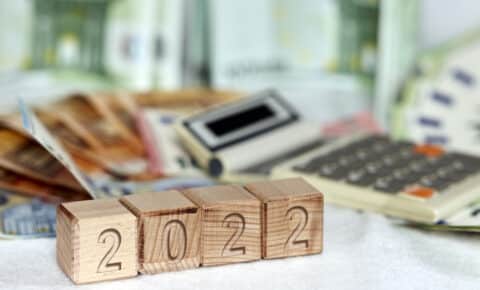 Vier Holzklötze formen "2022". Im Hintergrund sind Geldscheine und ein Taschenrechner zu sehen.
