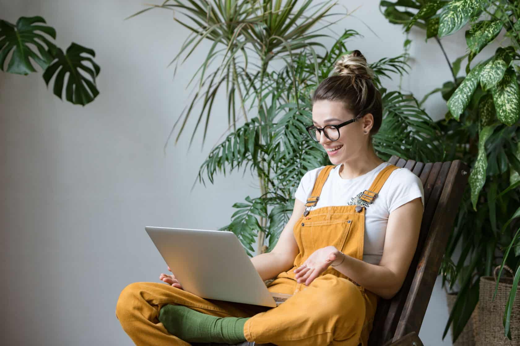 Junge Gärtnerin sitzt mit einem Laptop auf dem Schoß auf einem Stuhl