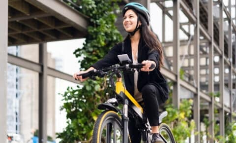 Eine junge Frau fährt Fahrrad in einer städtischen Umgebung. Sie trägt einen Helm und hat ihr Handy in einer Halterung am Lenker befestigt.