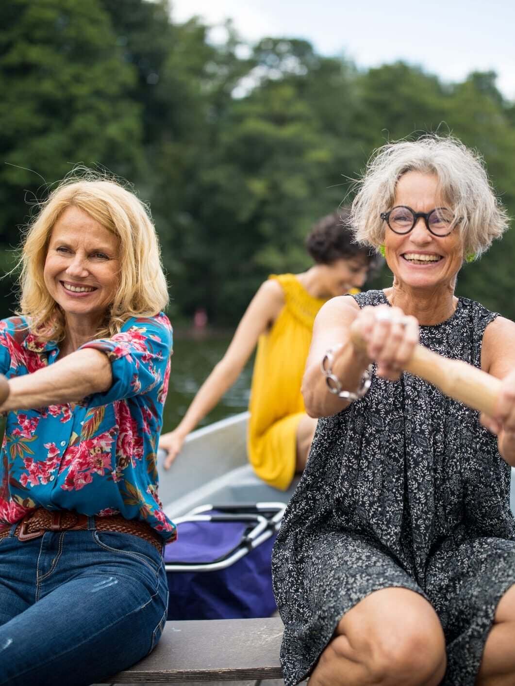 Drei Frauen unterschiedlichen Alters rudern lachend am Ufer eines Sees